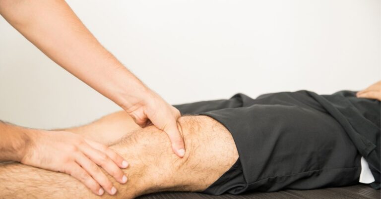 Physiotherapist Applying Pressure To Massage Young Man's Knee